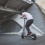 man in white t-shirt riding black and red kick scooter on gray concrete road during
