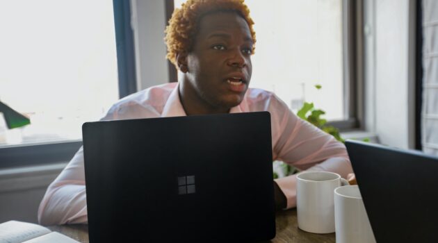 Person sitting at a desk behind a black Surface laptop