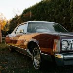 Vintage maroon car parked outdoors near trees.