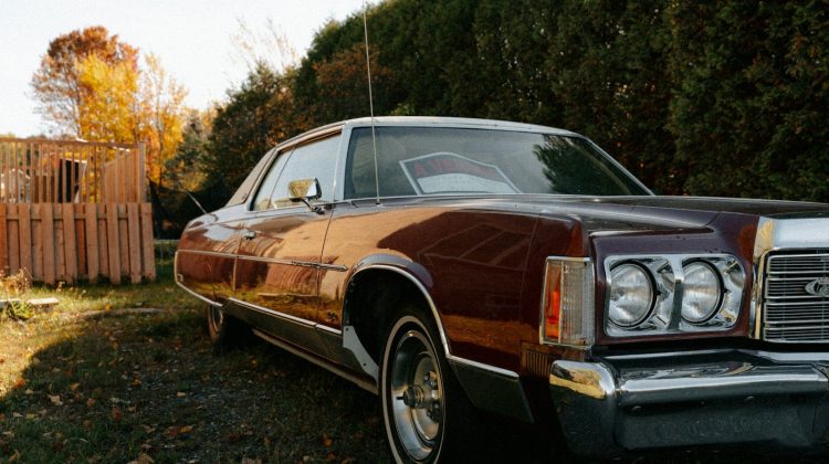 Vintage maroon car parked outdoors near trees.